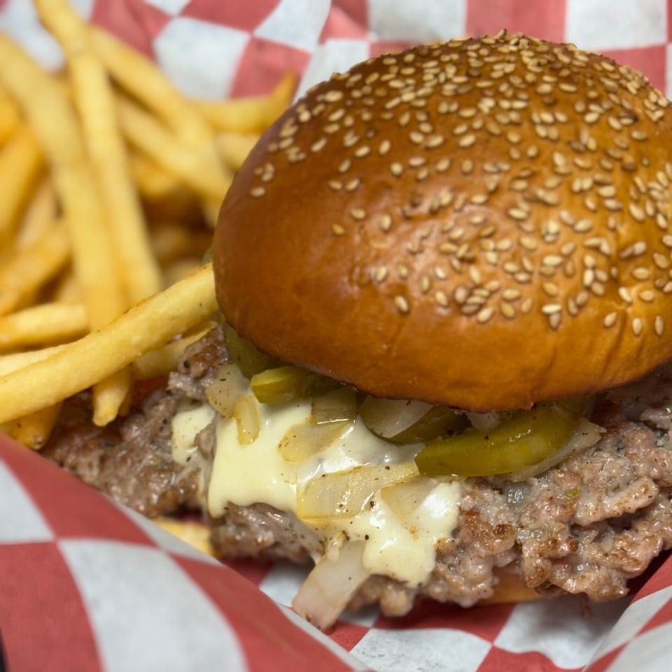 A Pitchers Pub burger with melted cheese, onions, and peppers, served with fries in a red checkered basket.