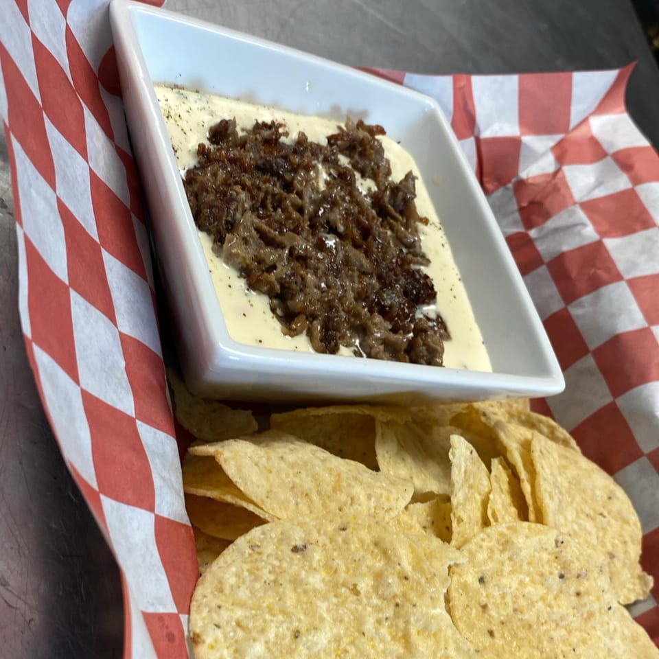 Pitchers Pub's Philly Cheesesteak Dip with tortilla chips in a red and white checkered basket.