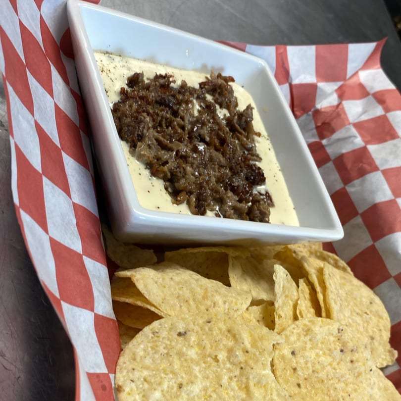 Pitchers Pub's Philly Cheesesteak Dip with tortilla chips in a red and white checkered basket.